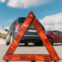 Czerwony trójkąt ostrzegawczy na drodze przed dwoma samochodami.