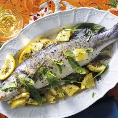Un succulento branzino in padella, guarnito con spicchi di limone e foglie di salvia, pronto per essere gustato.