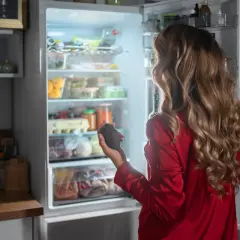 Kobieta w czerwonej piżamie trzyma awokado, zastanawiając się, na ile stopni ustawić lodówkę i zamrażarkę, by zachować świeżość produktów.