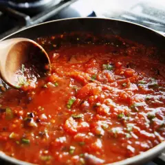 En träsked rör i en bubblande tomatsås i en stekpanna. Perfekt för ett enkelt tomatsås recept.