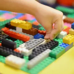 Kind baut mit bunten LEGO-Steinen. Viele LEGO-Ideen zum Nachbauen sind hier zu sehen, von einer Hand, die einen Stein platziert.