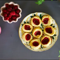 Hallongrottor recept: småkakor med hallonsylt på en vacker tallrik, bredvid en skål med färska hallon och en burk sylt.