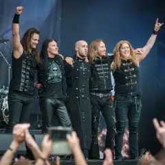 Zespół Beast in Black na koncercie, pięciu muzyków w czarnych strojach pozuje na scenie.