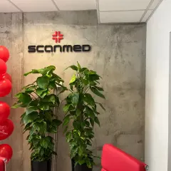 Czerwone balony i logo "Scanmed" na betonowej ścianie, obok zielonych roślin.