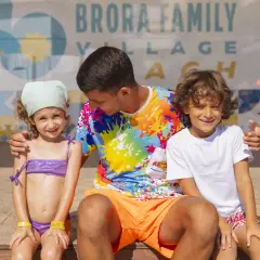 Un uomo con due bambini sorridono davanti a uno sfondo con la scritta "Brora Family Village".