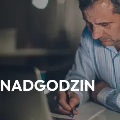 Mężczyzna pracuje po godzinach, rozliczając nadgodziny. Na ekranie laptopa widać napis "Rozliczanie nadgodzin".