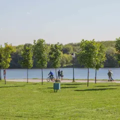 Spacer po alejkach nad zalewem nowohuckim. Ludzie spacerują, jeżdżą na rowerze, ciesząc się słońcem i zielenią.