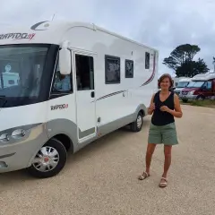 Une femme pose devant son camping-car Rapido, sur une aire de camping-car près de la Côte de Granit Rose.