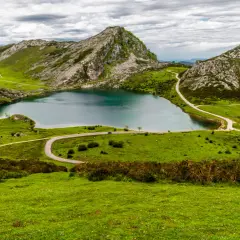 Lago en Picos de Europa que ver: paisaje verde con montañas rocosas, un lago azul y carreteras sinuosas.
