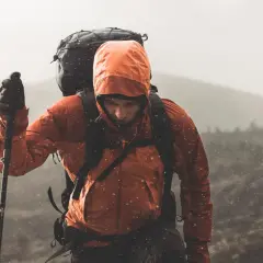 Turysta w pomarańczowej kurtce z kapturem i plecakiem wspina się po górach. Deszczowe Tatry szlaki na deszczowe dni nie straszne.