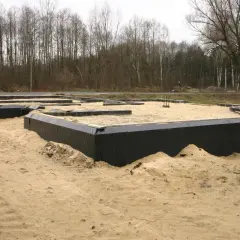 Fundamenty domu w piasku, otoczone czarną folią. W tle las. Wkrótce powstanie tu chudy beton.