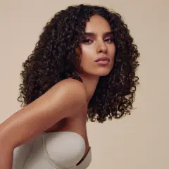 Descubre cómo peinar pelo rizado con esta modelo de cabello oscuro y voluminoso. Su melena luce definida y brillante, perfecta para cualquier ocasión.