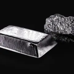 Sztabka i bryła platyny, najdroższego metalu na świecie, lśnią na czarnym tle.