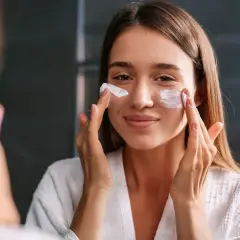 Kobieta w białym szlafroku nakłada kremy spf na twarz, dbając o ochronę skóry przed słońcem.