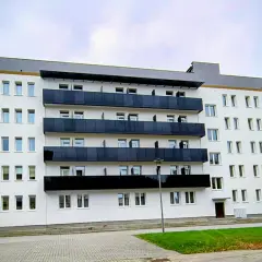 Nowoczesny budynek sanatorium uzdrowiskowego z białymi ścianami i czarnymi balkonami. W tle błękitne niebo.