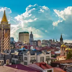 Widok na stolicę Adżarii, Batumi, z charakterystyczną wieżą zegarową i złotymi kopułami cerkwi pod błękitnym, chmurnym niebem.
