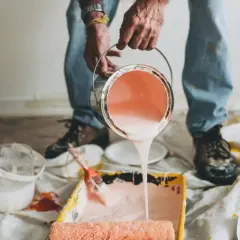 Mani versano pittura rosa da una latta in una vaschetta per rulli. Impara come diluire la pittura per un lavoro perfetto.