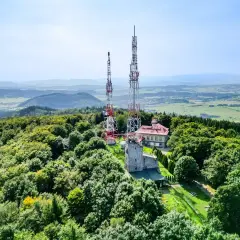 Wieże telekomunikacyjne na zalesionym szczycie Chełmiec. W tle rozległa panorama krajobrazu.