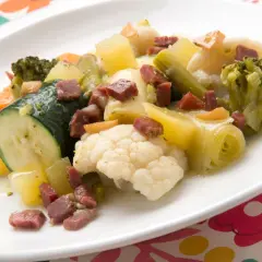 Un colorido panache de verduras con brócoli, coliflor, calabacín, zanahoria y patatas, salpicado de trocitos de jamón.