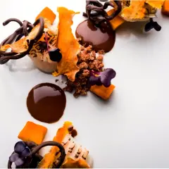 Postre de autor con chocolate, naranja y flores moradas. Una obra de arte culinaria que promete una experiencia gastronómica inolvidable.