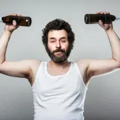 Mężczyzna w białej podkoszulce podnosi dwie butelki, symbolizując wpływ testosteronu a alkoholu na siłę i samopoczucie.