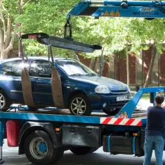 Une dépanneuse charge une voiture bleue. Si vous vous demandez comment savoir si ma voiture est à la fourrière, regardez si elle disparaît de là où vous l'avez garée.