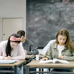 Uczniowie skupieni na zadaniach. Dziewczyna pisze, druga czyta. W tle tablica. Kiedy skończą, będą wiedzieć, jak budowa future perfect simple.
