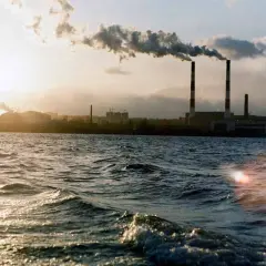 Chimeneas industriales emiten humo sobre un río, un ejemplo de cómo se mide la calidad del aire.