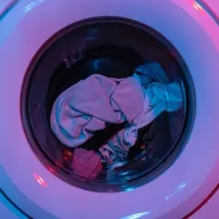 Ein Wäschekorb voller Kleidung, darunter auch AirPods, wartet auf die Waschmaschine.