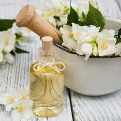 Jasminöl in einer Flasche, umgeben von Blüten. Die Jasmin Wirkung auf die Psyche ist beruhigend und stimmungsaufhellend.
