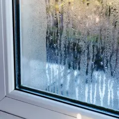 Gouttes d'eau ruisselant sur une fenêtre, signe de condensation. La lumière du jour filtre à travers les gouttelettes.