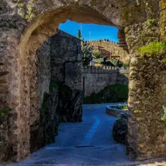 Un pasaje de piedra antigua nos lleva a descubrir lugares secretos de la Sierra de Madrid, con un camino empedrado y murallas que evocan historia.