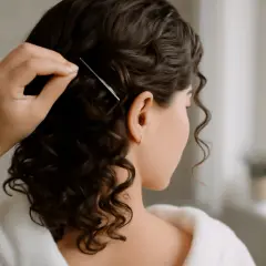 En kvinna med mörkt, lockigt hår använder en kam för att styla sitt hår. Hon ser ut att förbereda sig för att våffla håret för en festlig look.