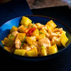 Patatas bravas receta: trozos dorados de patata cubiertos con una cremosa salsa rosada y decorados con pimiento rojo y cebolleta.
