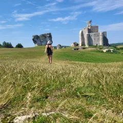Kobieta w kapeluszu idzie przez łąkę w kierunku ruin zamku na Szlaku Orlich Gniazd.