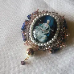 Broche con camafeos, perlas y detalles florales. Una dama elegante lee un libro en un retrato ovalado, rodeada de encaje y cristales.
