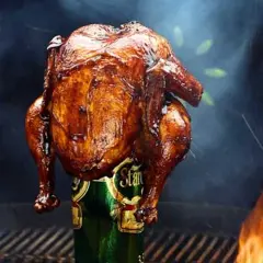 En saftig, gyllene hel kyckling tillagas stående på en ölburk, omgiven av rök och flammor. En klassisk beer can chicken.