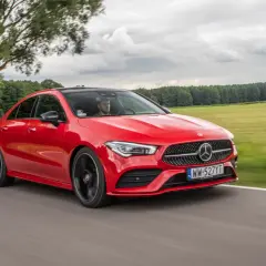 Czerwony Mercedes-Benz CLA Coupe pędzi po drodze wśród zielonych pól i drzew.