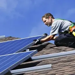 Installatore sul tetto, con imbracatura, che fissa pannelli fotovoltaici. L'orientamento dei pannelli è cruciale per massimizzare l'energia solare.