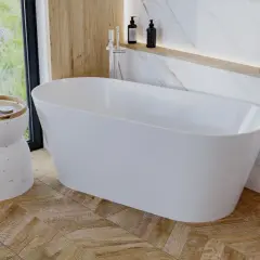 Elegancka wolnostojąca wanna w łazience z drewnianą podłogą ułożoną we wzór jodełki. Obok wanny stoi stolik z kosmetykami i kwiatami.
