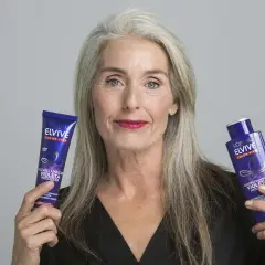 Mujer con cabello gris muestra productos Elvive Color-Vive, ideales como remedios caseros para quitar el amarillo del pelo y matizar.