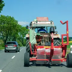 Ein Traktor mit Ballenwickler fährt langsam auf der Autobahn. Ein Auto dahinter gibt Lichthupe, um zu überholen.