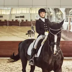 Elegancka amazonka w frakach jeździeckich na czarnym koniu w ujeżdżalni.