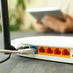 Router z podłączonym kablem Ethernet i portami LAN. W tle osoba z tabletem.