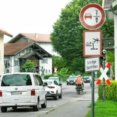 Verkehrszeichen 277 weist auf schräge Spurrillen hin. Ein Radfahrer wird gezeigt, der fast stürzt. Autos und Radfahrer fahren auf einer Straße.