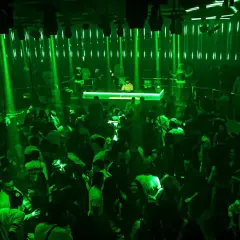 A crowded nightclub with green lights and a DJ booth.