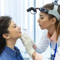Lekarz laryngolog bada pacjentkę z nawracającą chrypką, używając otoskopu.