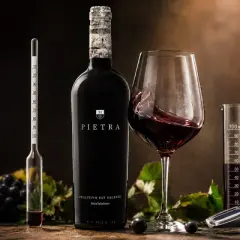Butelka wina Pietra, kielich z czerwonym winem, winogrona i przyrządy do pomiaru alkoholu. To wino 18 procent, idealne do degustacji.