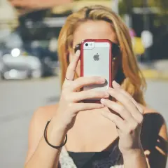 Kobieta z blond włosami trzyma iPhone'a, być może wykonując twardy reset.