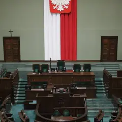 Pusta sala sejmowa z rzędami zielonych foteli i mównicą. Biało-czerwona flaga i godło Polski. Zastanawiasz się, ile jest posłów w sejmie?